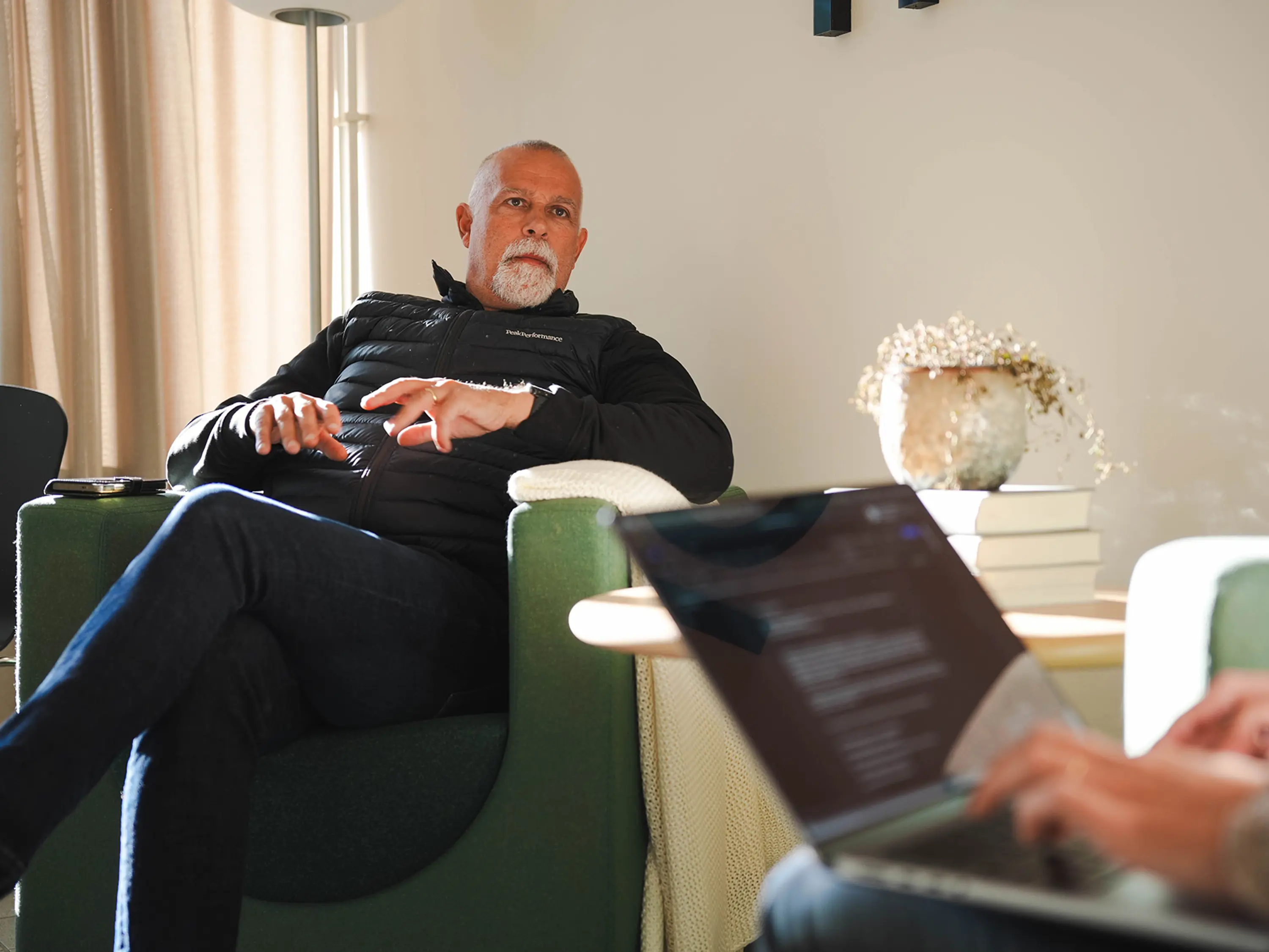 Man i fotölj som blir intervjuad av en annan person med laptop i knät
