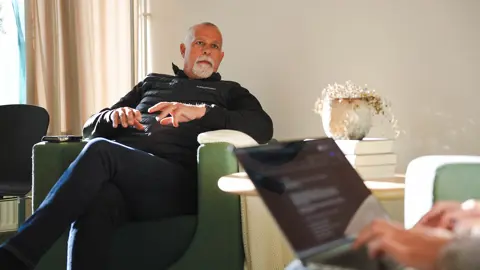 Man i fotölj som blir intervjuad av en annan person med laptop i knät