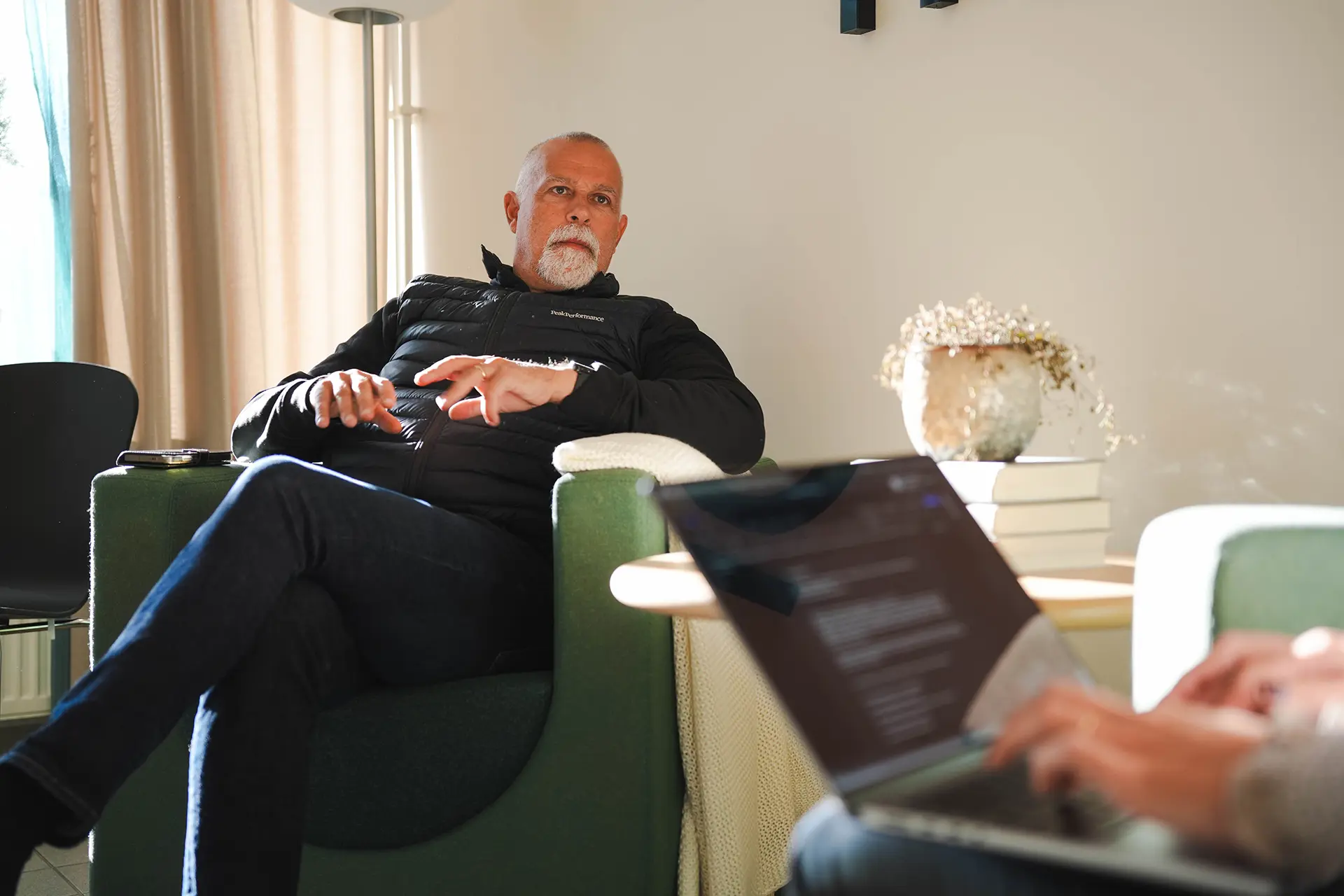 Man i fotölj som blir intervjuad av en annan person med laptop i knät