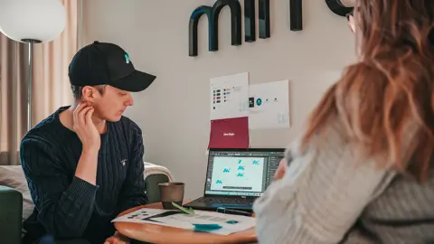 Två personer som sitter vid ett runt bord och tittar på en dator med designelement